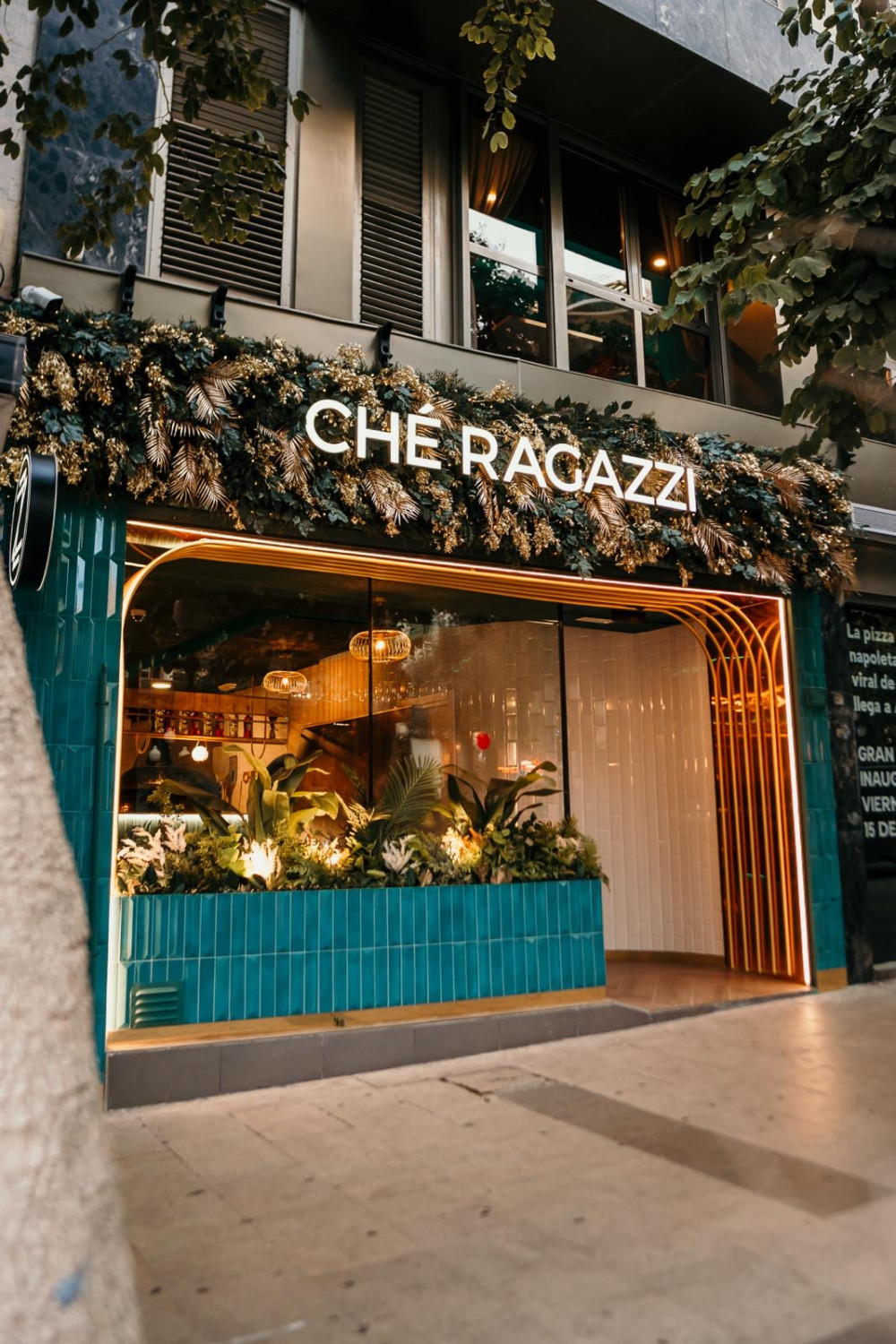 Fachada del restaurante Ché Ragazzi con follaje artificial y jardineras turquesa