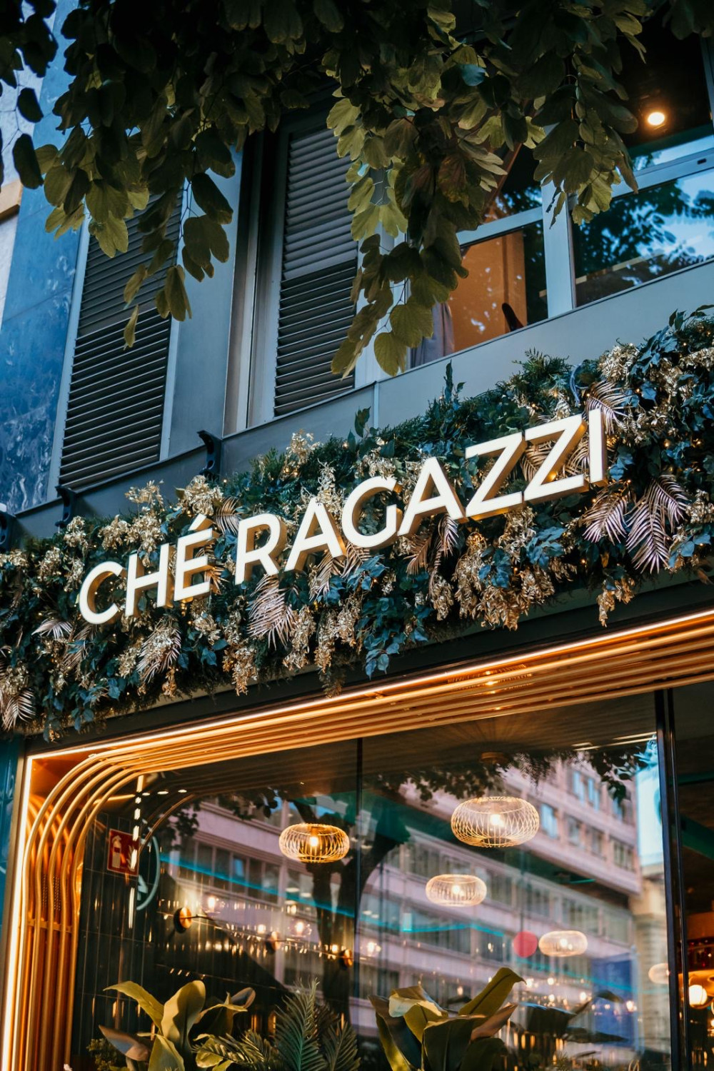 Fachada del restaurante Ché Ragazzi con vegetación artificial sobre el rótulo iluminado