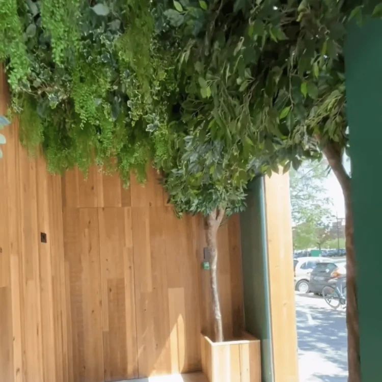 Árbol artificial de hoja verde junto a una pared de listones de madera