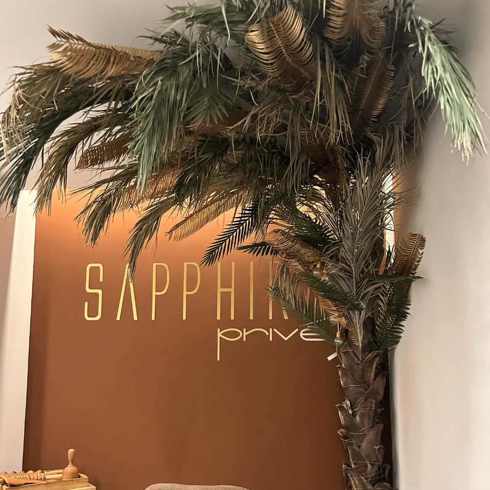 Palmeras artificiales junto al rótulo dorado de Sapphire Privé