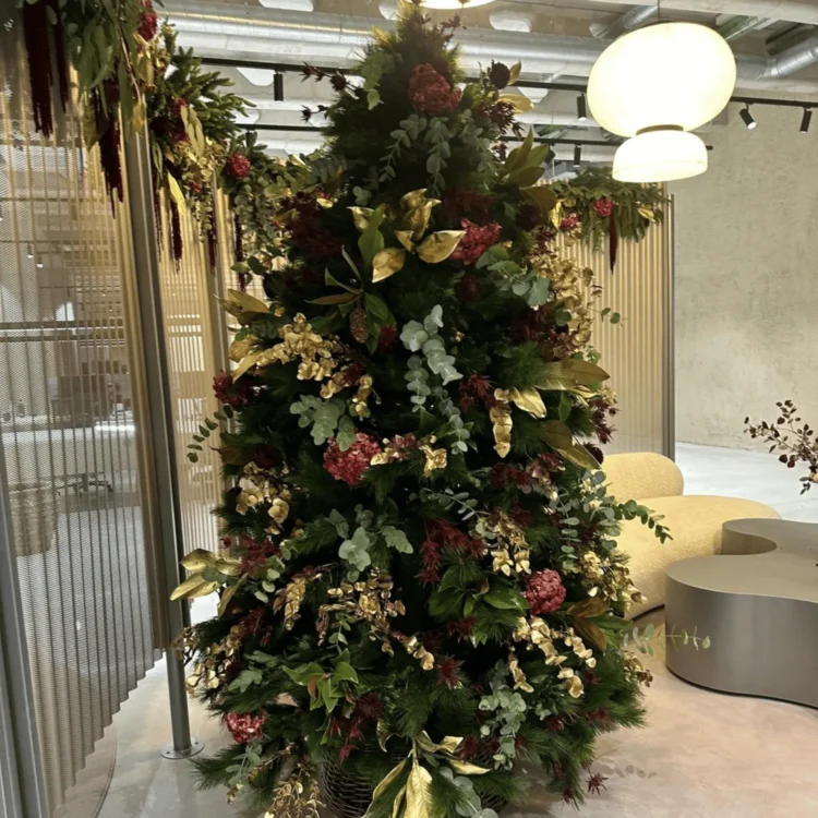 Árbol de Navidad artificial de gran tamaño con follaje granate y dorado en un espacio comercial