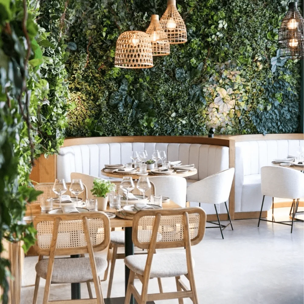 Comedor de restaurante con la pared cubierta de jardín vertical artificial y lámparas de fibra