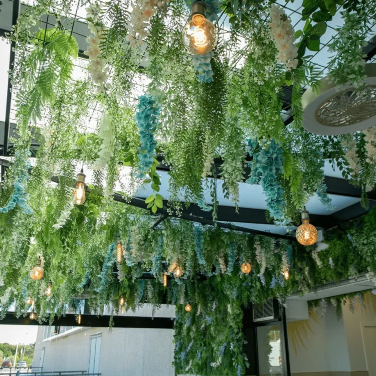 Techo cubierto de plantas colgantes artificiales y bombillas vintage en una terraza