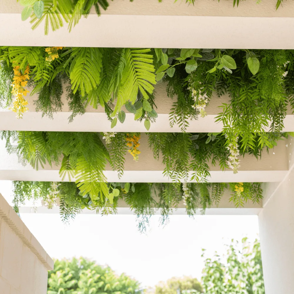 Pérgola con plantas colgantes artificiales sobre las vigas blancas