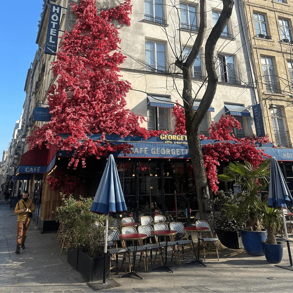 Fachada de un café decorada con flores artificiales fucsia sobre la terraza