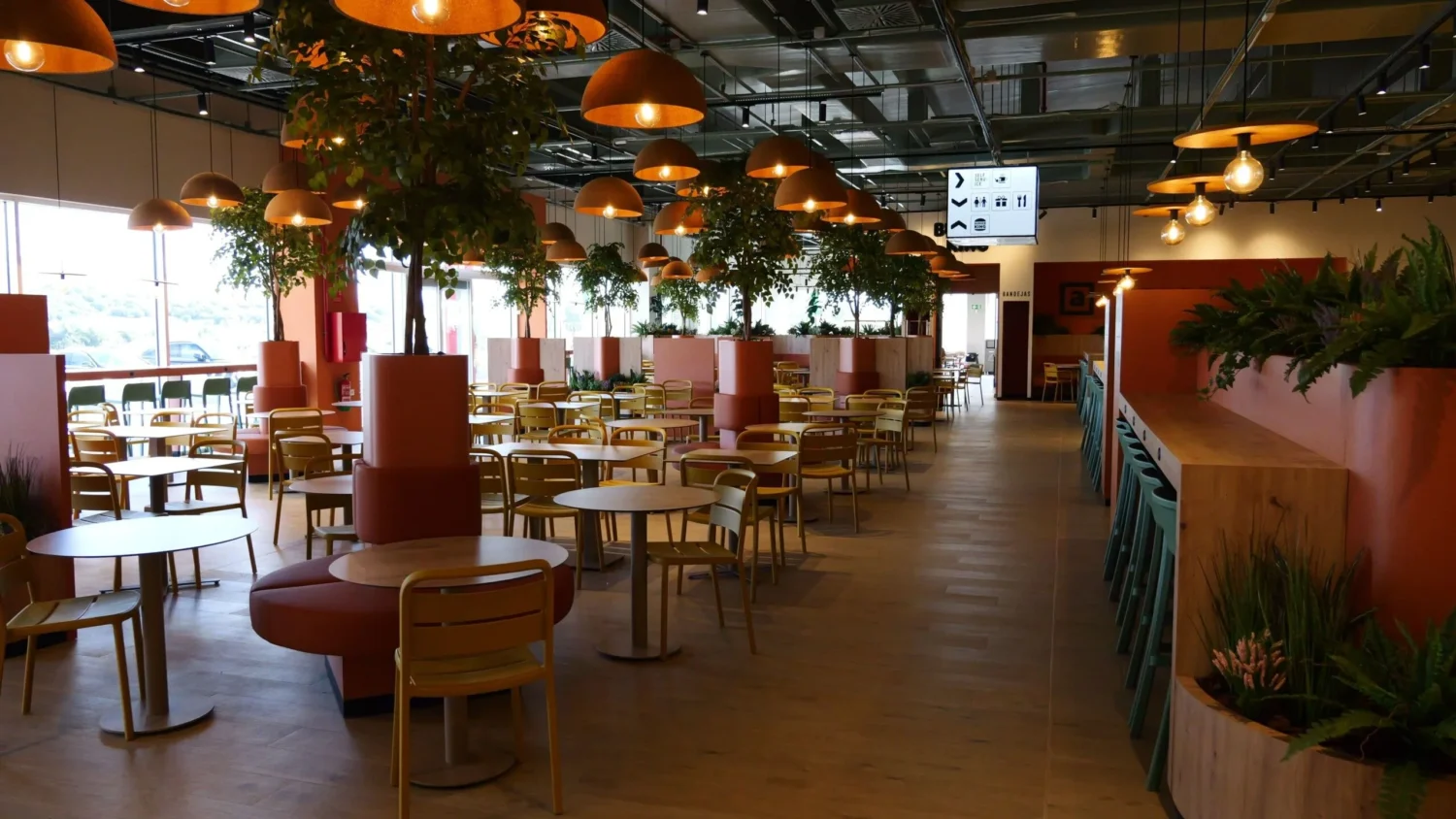 Comedor del área de servicio Abades Los Gazules con árboles artificiales entre las mesas
