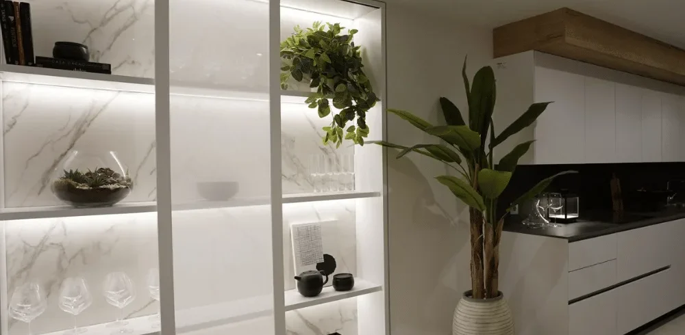 Plantas artificiales en la estantería iluminada y en el suelo de una cocina blanca