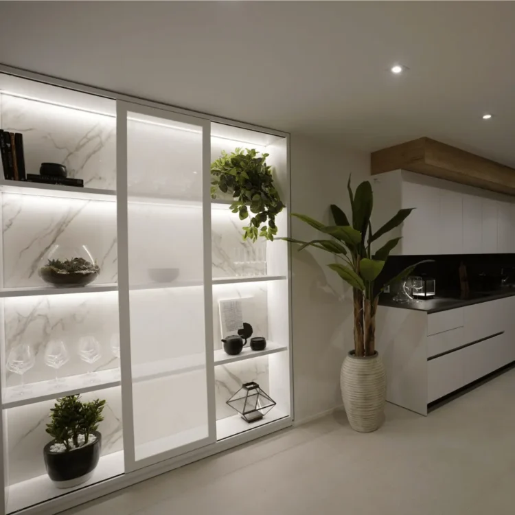 Plantas artificiales en la estantería iluminada y en el suelo de una cocina blanca