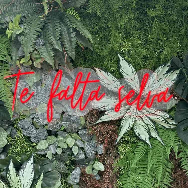 Jardín vertical artificial con helechos y un rótulo de neón que dice Te falta selva