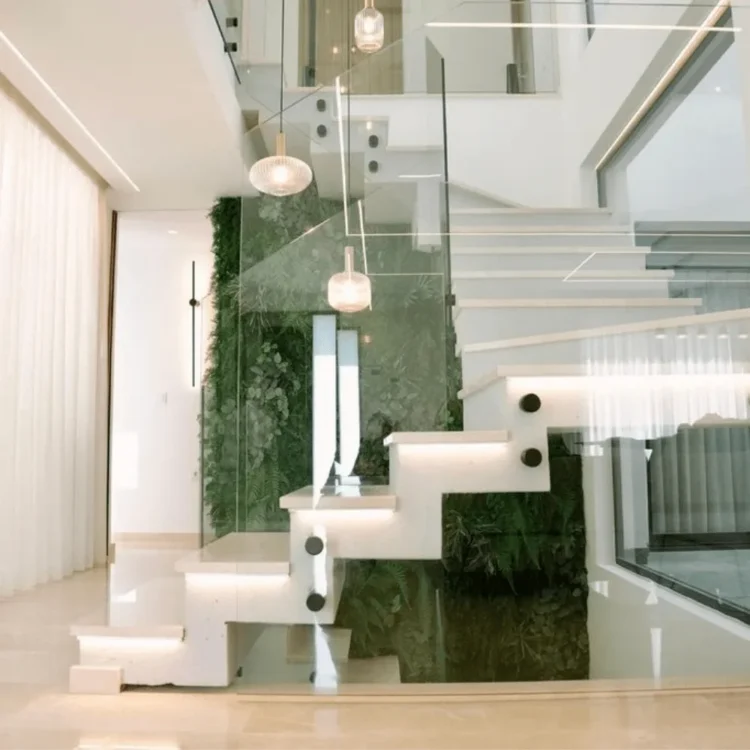 Pared verde artificial junto a la escalera de una vivienda contemporánea con barandilla de cristal