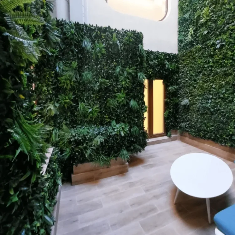 Patio interior con jardín vertical artificial cubriendo las paredes y mobiliario blanco