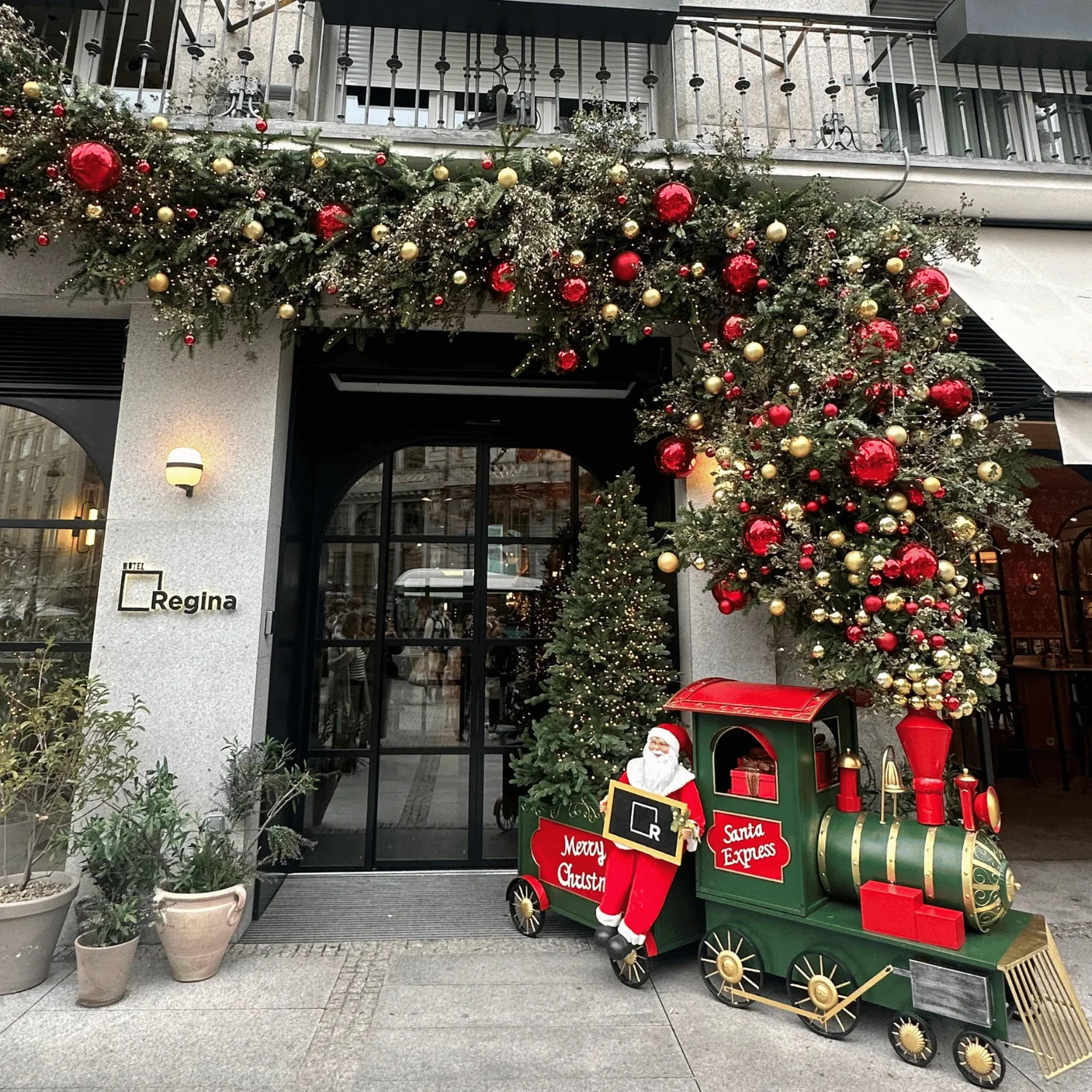 Entrada de un hotel decorada en Navidad con vegetación, bolas y un tren