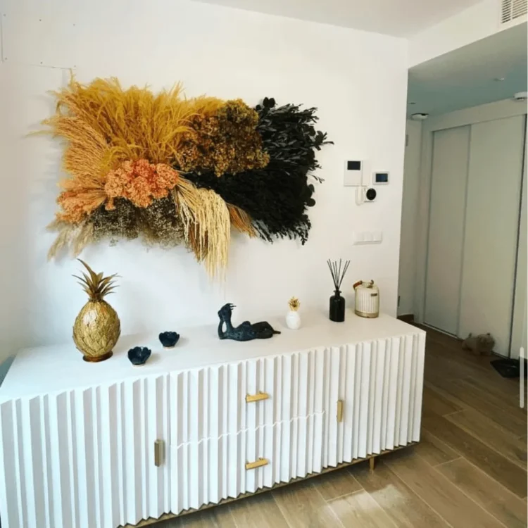 Cuadro de plantas preservadas en tonos ocre sobre un aparador blanco