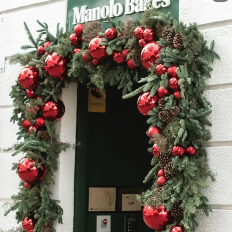 Arco navideño de vegetación artificial con bolas rojas enmarcando la puerta de un local
